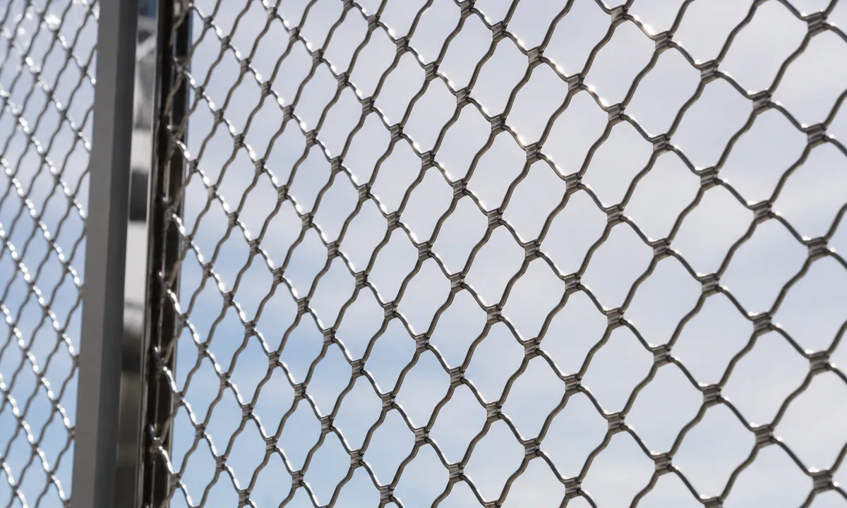 Photograph: fine metal security mesh in daylight—neutral industrial texture, calm exposure.
